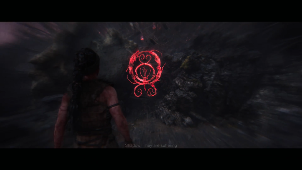 Senua approaches glowing red rune in dark cave