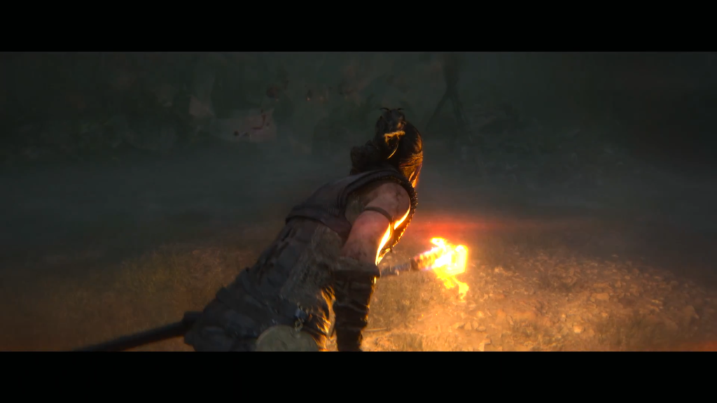 Senua holds glowing torch in dark forest, Hellblade