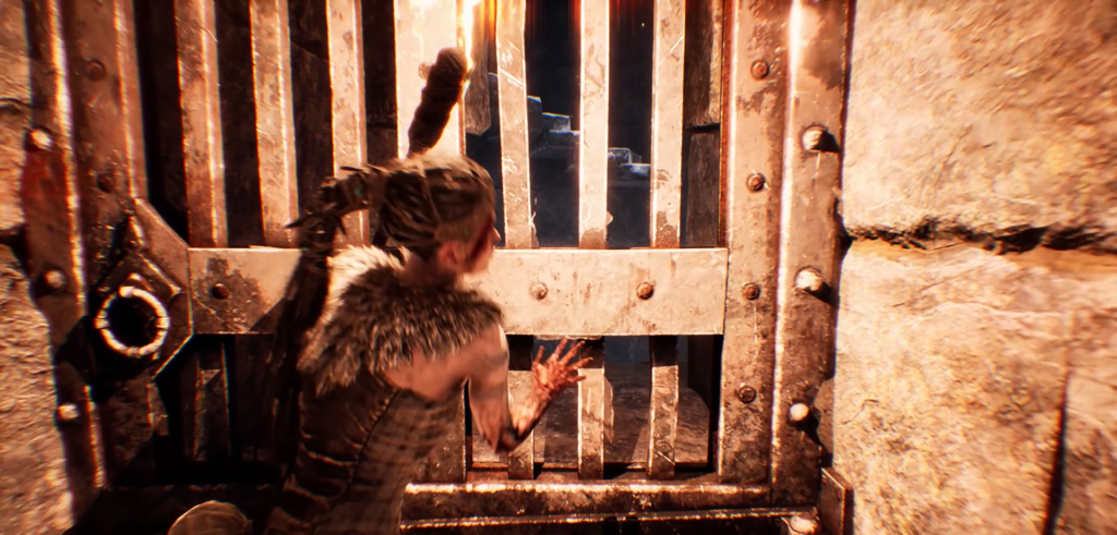 Senua pushes metal gate in stone corridor