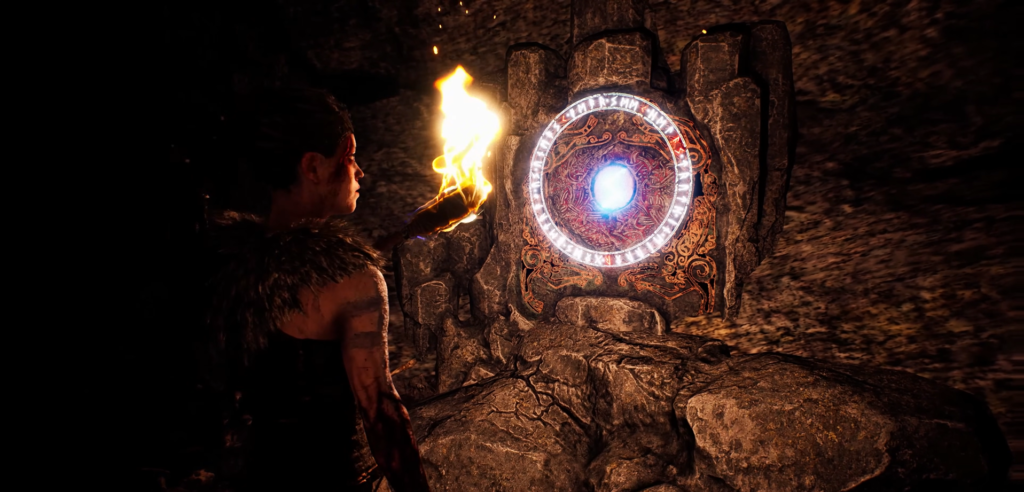 Senua holds torch facing glowing rune portal in cave