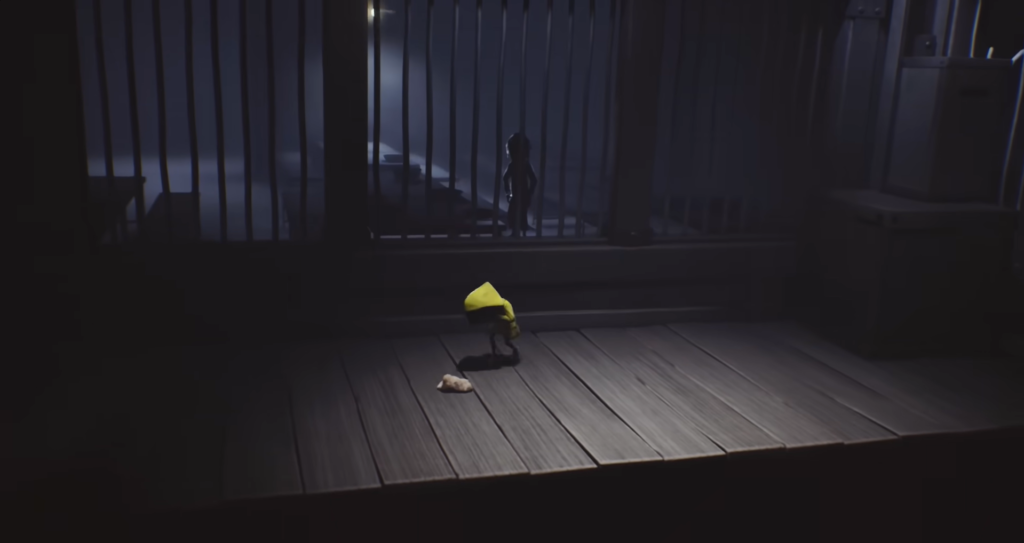 Six from Little Nightmares crouches on wooden floor near bars