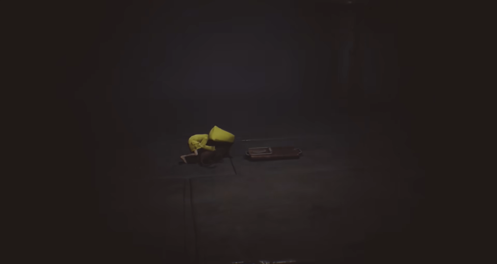 Six from Little Nightmares crouches beside suitcase in darkness