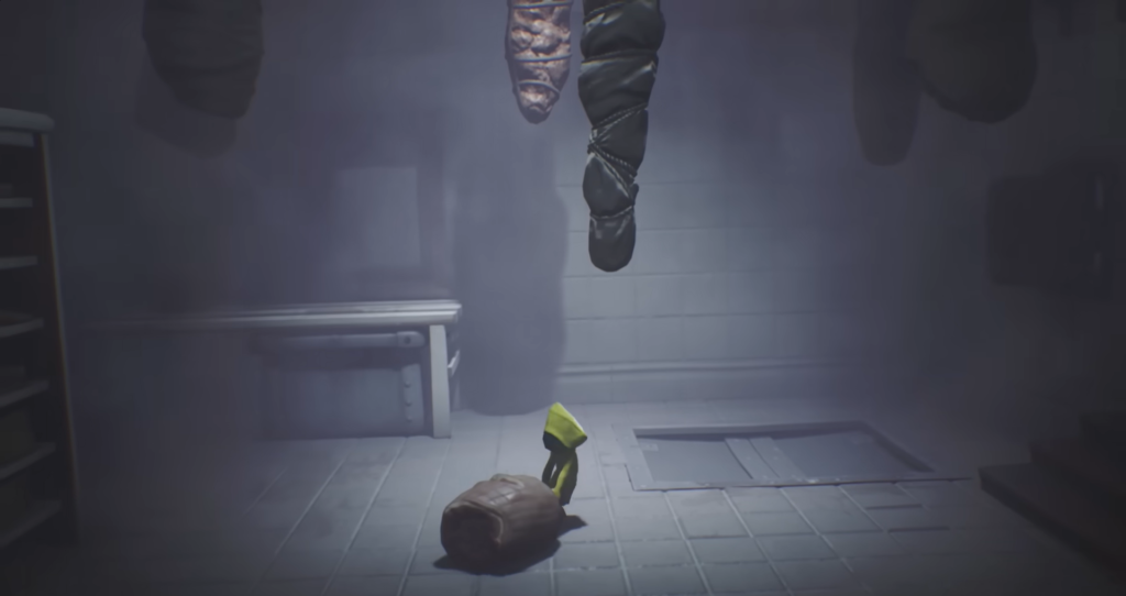 Six from Little Nightmares stands under hanging bodies indoors