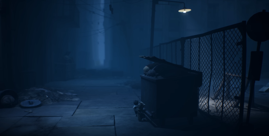 Small figure crouches beside dumpster in dark alley